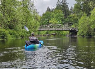 man in a blue sit-in kayak on the Black River. A bridge over the river can be seen in the distance
